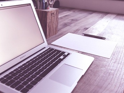 Laptop, daneben Blatt mit Stift