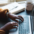 Frau vor Laptop mit Notizbuch und Kaffee