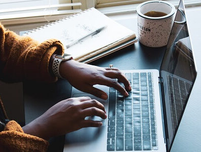 Frau vor Laptop mit Notizbuch und Kaffee